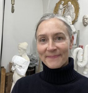 White woman, 50s, long gray hair in a ponytail, wearing a black turtleneck.