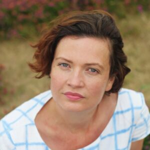 white woman, mid 40s, short dark hair wearing and white shirt looking into the camera